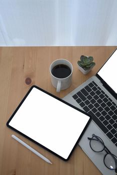 Modern workplace with laptop, digital tablet, coffee cup and glasses one wooden table.