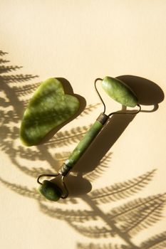 Jade Gua sha scraper and facial massager on beige background. Hard light, shadows, the concept self-care. Facial care. Zero waste. Lifting and toning treatment at home.