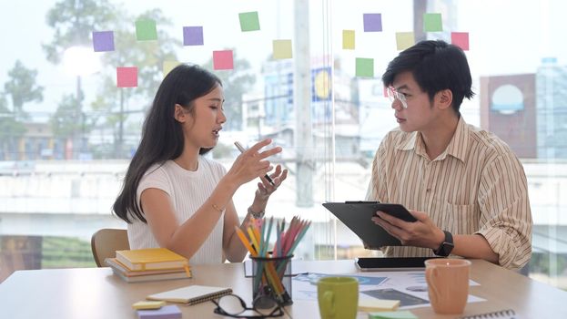 Focused young woman and her colleague are discussing new marketing strategy together.