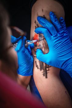 Master demonstrates the process of getting tattoo in tattoo studio./Tattooist at work in his salon.