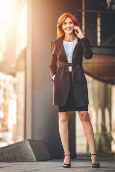 Smiling successful business woman is talking on smartphone in office district.