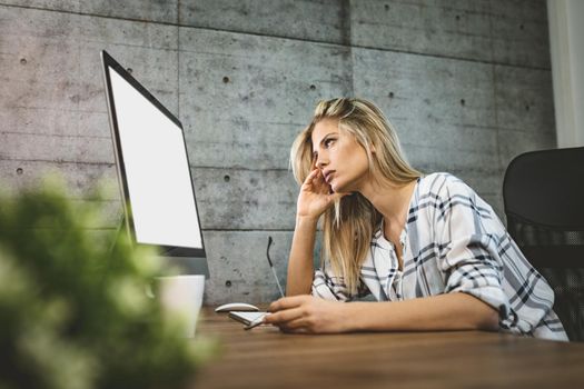 Young handsome frustrated and stressed business woman sitting at the office front a computer and holding head.