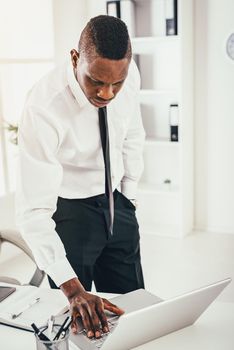 Pensive African businessman is working on laptop in modern office and planning what to do next.