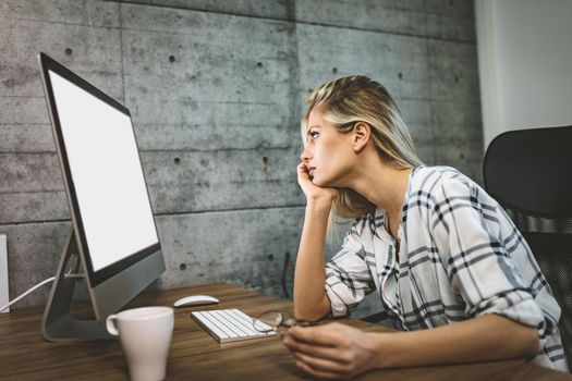 Young handsome frustrated and stressed business woman sitting at the office front a computer and holding head.