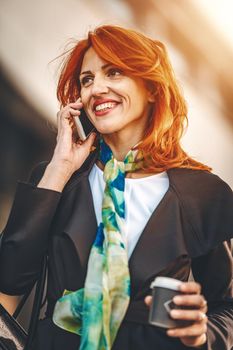 Smiling successful business woman is talking on smartphone in office district.