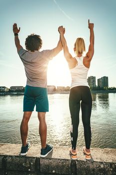 A beautiful young couple is standing on a wall beside the river and greeting the sun after training.