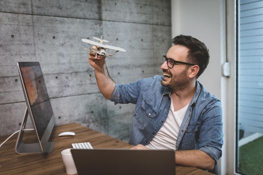 Young handsome successful smiling freelance entrepreneur having fun and showing little model of airplane, explaining how it flies.