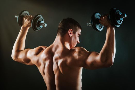 Rear view of a perfect muscular man is performing exercise with dumbbells.