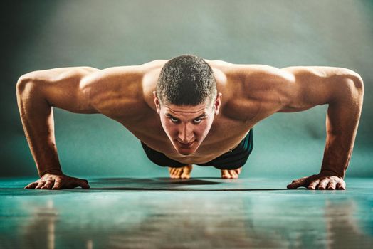 Young strong shirtless muscular man is exercising push ups indoors. 