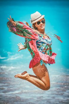 Beautiful young woman in colorful dress is playing in the shore on the beach during the hot summer vacation day. She is enjoying and jumping on the beach. 