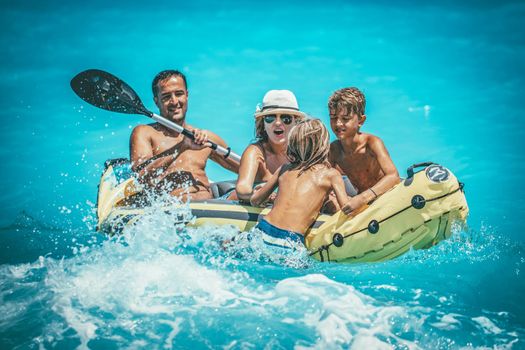 Happy family is enjoying paddling in yellow kayak at tropical ocean water during summer vacation.They are kayaking on the sea.