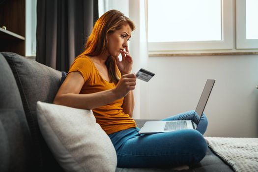 Shot of a worried young woman doing online shopping on her laptop while sitting on the sofa at home.