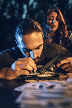 A criminal young man drug addict sniffs a cocaine track with a rolled-up note. 