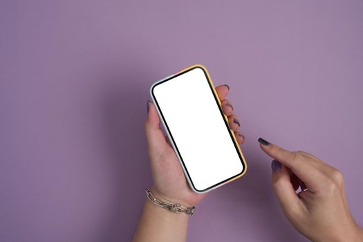 Woman hand using smart phone on purple background. Empty screen for graphic display montage.