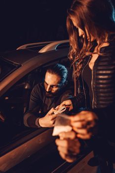 The dealer sells a little bag of heroin or cocaine to a young woman from a car, and she gives him money.