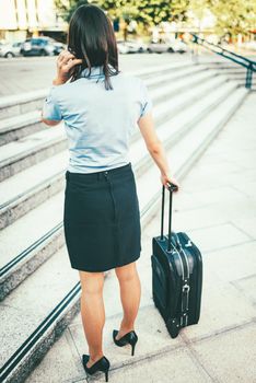 Young beautiful businesswoman standing outdoor with suitcase ready for a business trip.