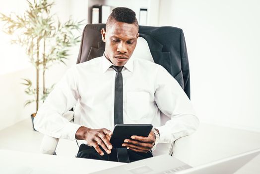 Pensive African businessman working on digital tablet in modern office.