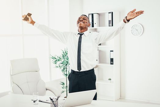 Successful African businessman celebrating success with raised arms in the modern office.