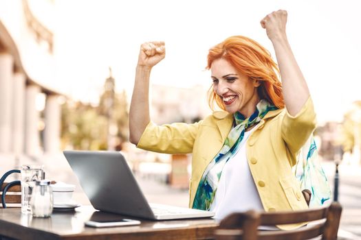 Successful business woman received good news using laptop on a coffee break in a street cafe.