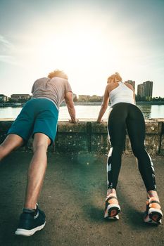 Young happy smiling couple is training outdoors doing push-ups during outdoor cross training by the river.