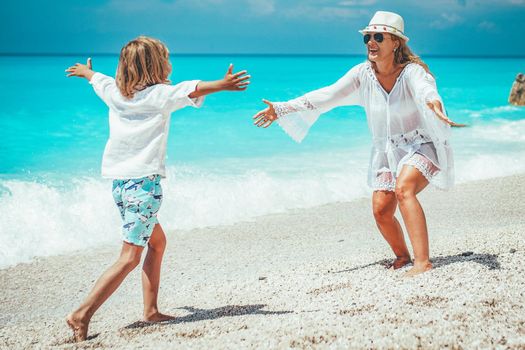 Beautiful little boy enjoying with his mother on the beach. He is running along the beach into his mother's arms.