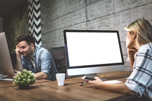 Young successful freelance designers working at the office. They are analyzing project on a computer and thinking about it.