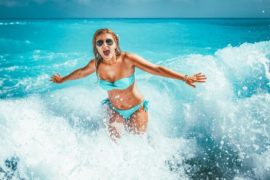 A young woman having fun in the waves of the sea which are splashing her.
