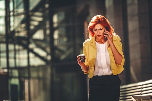 Stressed business woman is talking on smartphone in office district.