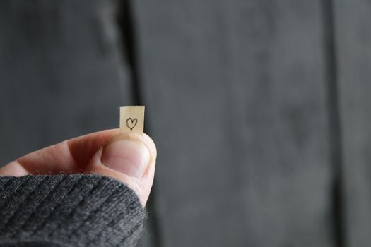 Male hand holding a smoll paper card with heart symbol drawing.