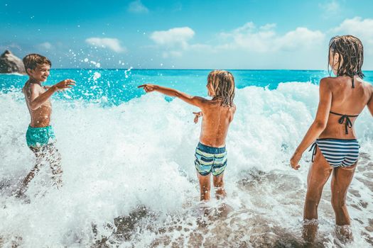 Brothers and sister playing in the shore on the beach during the hot summer vacation day.