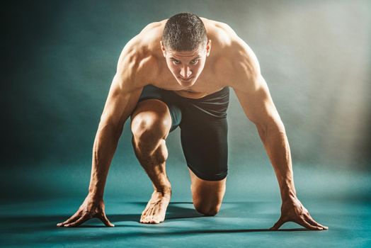 Strong muscular man is kneeling on the floor  like sprinter starting position. 