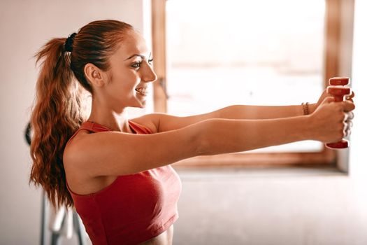 Beautiful young woman doing exercises with dumbbells at home.