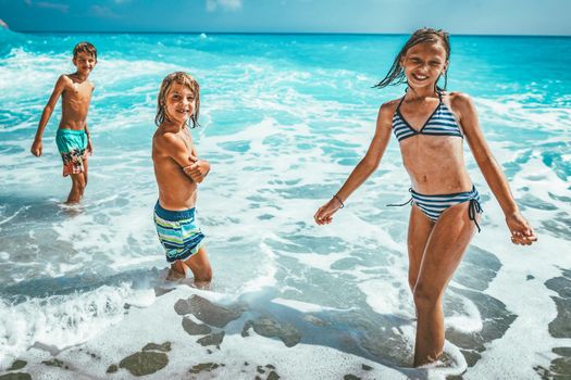 Brothers and sister playing in the shore on the beach during the hot summer vacation day.