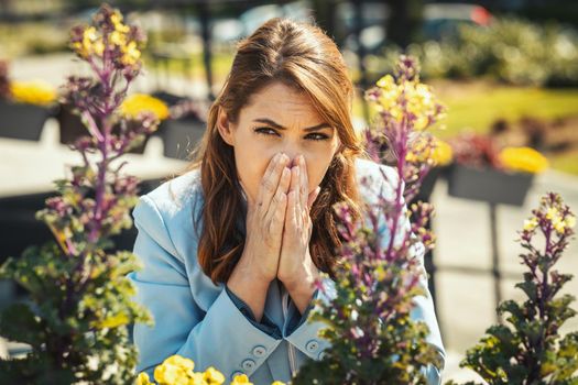 Young businesswoman on break outside sneezing due to allergies or colds.