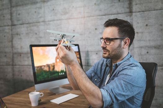 Young handsome successful freelance entrepreneur having fun and showing little model of airplane, explaining how it flies.