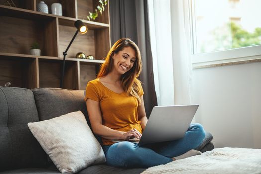 Shot of an attractive young woman sitting cross legged on the sofa and using her laptop at home.