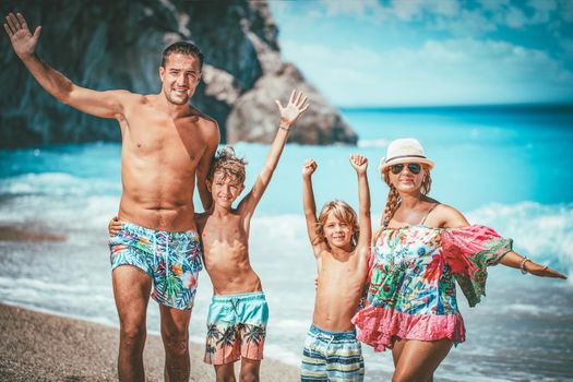 Young family with two sons are posing on the sea beach in summer day and looking at camera.