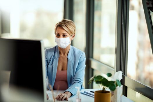 Business woman in a medical protective mask works at the office on the computer during self-isolation and quarantine to avoid infection during flu virus outbreak and coronavirus epidemic.