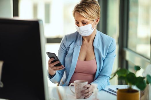 Business woman in a medical protective mask works from home at the computer, using smartphone, during self-isolation and quarantine to avoid infection during flu virus outbreak and coronavirus epidemic.