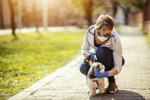 A woman in a medical protective mask is spending time and walking with her cute little Shih Tzu dog during allergy or flu virus outbreak and coronavirus epidemic.