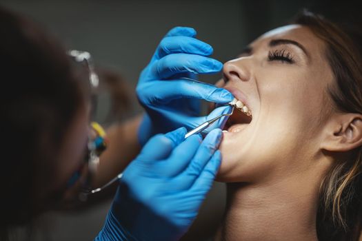 The beautiful young woman is at the dentist. She sits in the dentist's chair and the dentist sets braces on her teeth putting aesthetic self-aligning lingual locks.