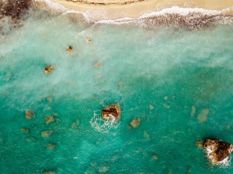 Aerial view from drone of the beautiful crystal clear turquoise and blue sea water, surrounding rocks and waves reaching sandy beach. 