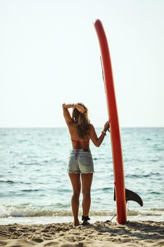 A young woman on a sea beach with a surfboard is ready for the waves.