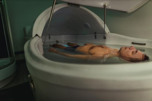 Relaxed man is floating in a sensory deprivation tank. He is very relaxed. Wellness and Spa concept.