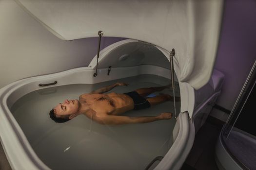 Relaxed man is floating in a sensory deprivation tank. He is very relaxed. Wellness and Spa concept.