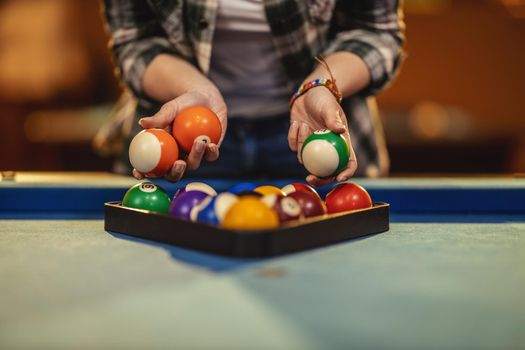 Close-up of a young woman's hands places billiard balls on a pool table to play.