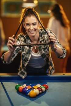 A young smiling woman places billiard balls on a pool table to play.