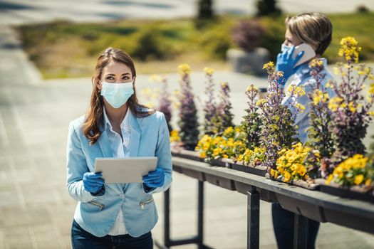 Young business woman with protective mask on her face is looking something on her digital tablet outdoor during COVID 19 pandemic.