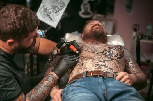 Tattooer working tattooing in tattoo parlour./Tattoo master works in the salon.