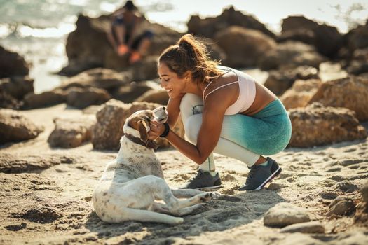 A beautiful young woman is petting her dear dog at the sea beach in summer sunny day.